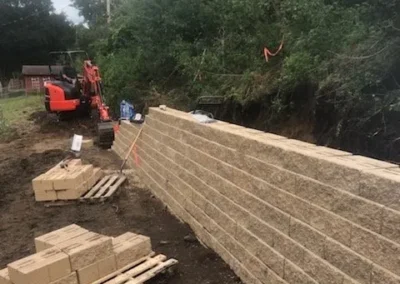 Construction site with a newly built beige retaining wall and mini excavator